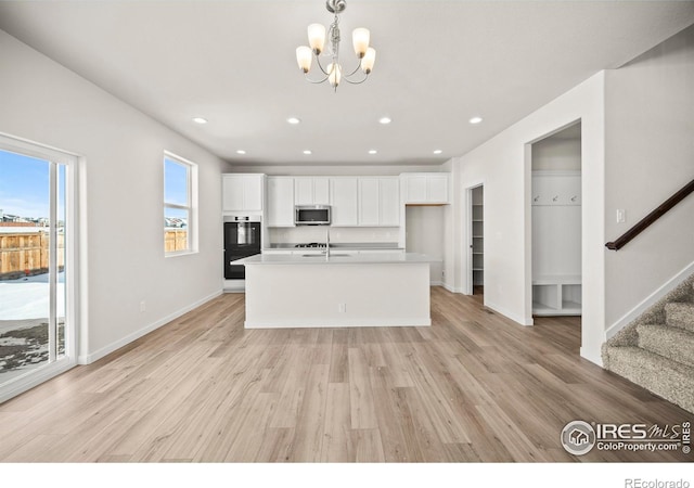 kitchen featuring an inviting chandelier, light hardwood / wood-style floors, double oven, a kitchen island with sink, and white cabinets