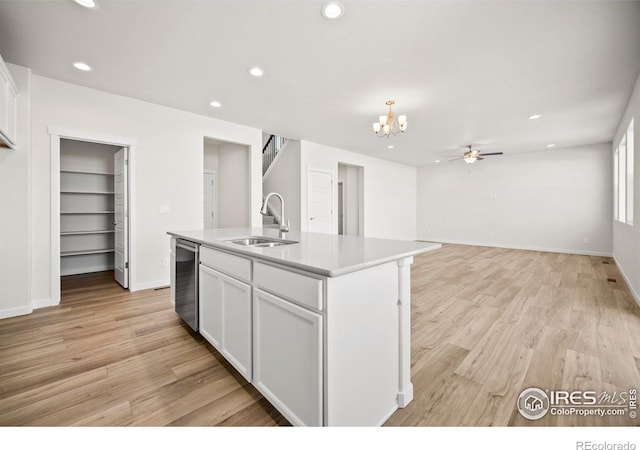 kitchen with ceiling fan with notable chandelier, white cabinetry, an island with sink, sink, and light hardwood / wood-style floors