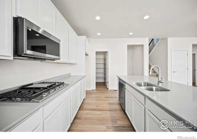 kitchen with stainless steel appliances, white cabinetry, sink, and light hardwood / wood-style flooring