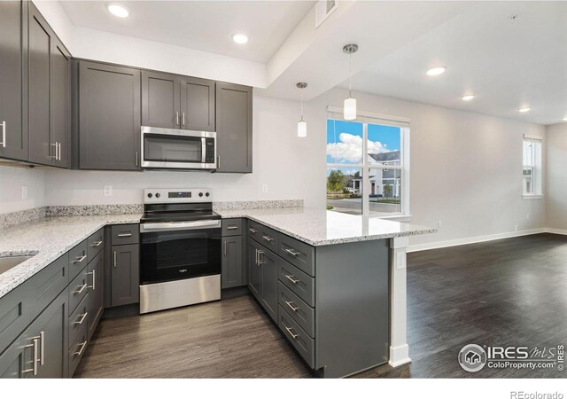 kitchen with appliances with stainless steel finishes, hanging light fixtures, kitchen peninsula, light stone countertops, and dark hardwood / wood-style flooring