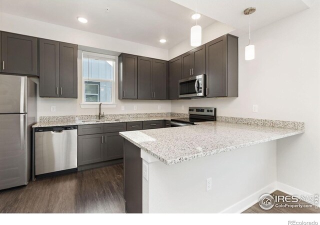 kitchen featuring hanging light fixtures, sink, kitchen peninsula, stainless steel appliances, and dark hardwood / wood-style floors