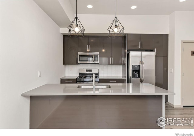 kitchen with pendant lighting, sink, backsplash, a kitchen island with sink, and stainless steel appliances