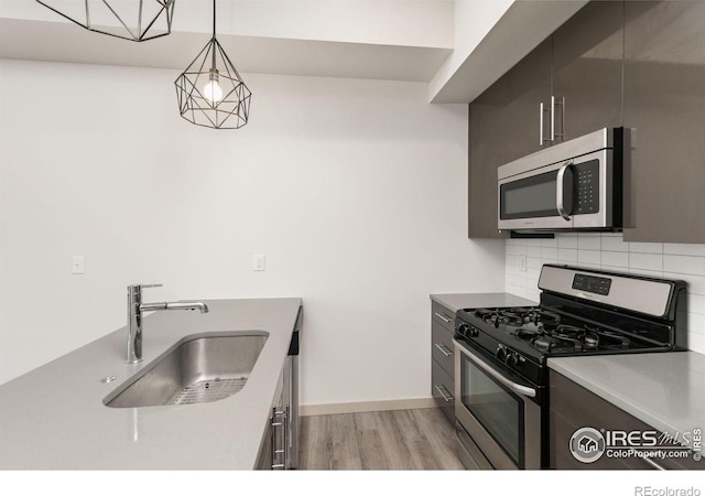 kitchen featuring sink, appliances with stainless steel finishes, hanging light fixtures, decorative backsplash, and light wood-type flooring