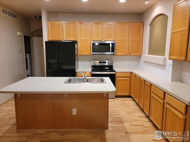 kitchen with light hardwood / wood-style flooring, stainless steel appliances, sink, backsplash, and a center island with sink