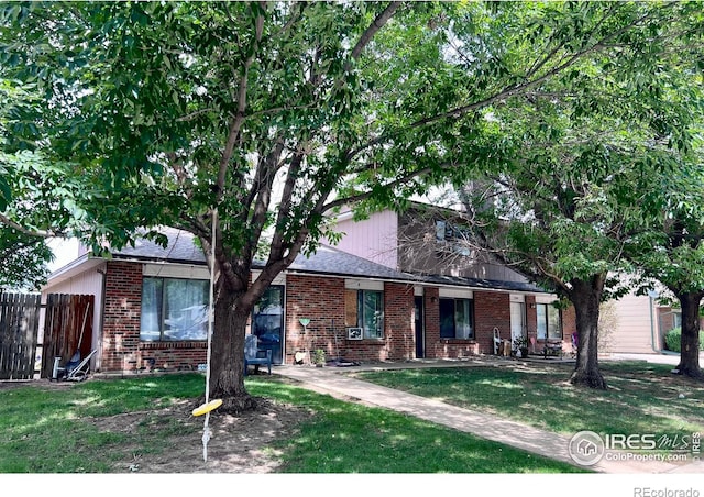 view of front of house featuring brick siding, a front lawn, and fence