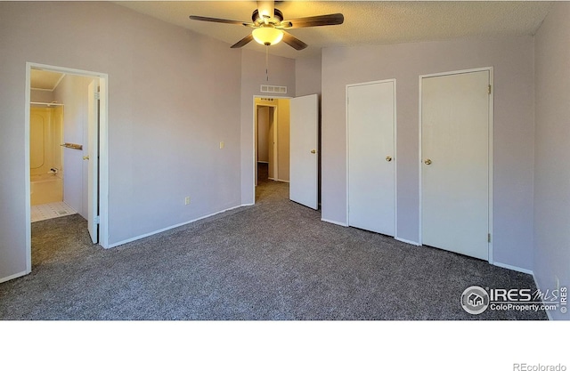 unfurnished bedroom featuring ceiling fan, vaulted ceiling, ensuite bath, and dark carpet