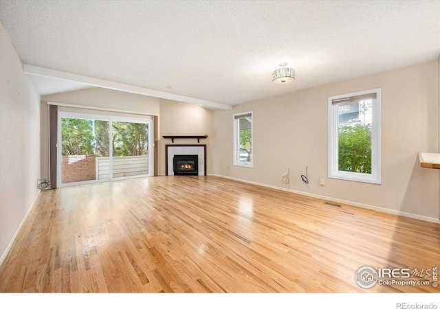 unfurnished living room with a healthy amount of sunlight, a fireplace, a textured ceiling, and light wood finished floors