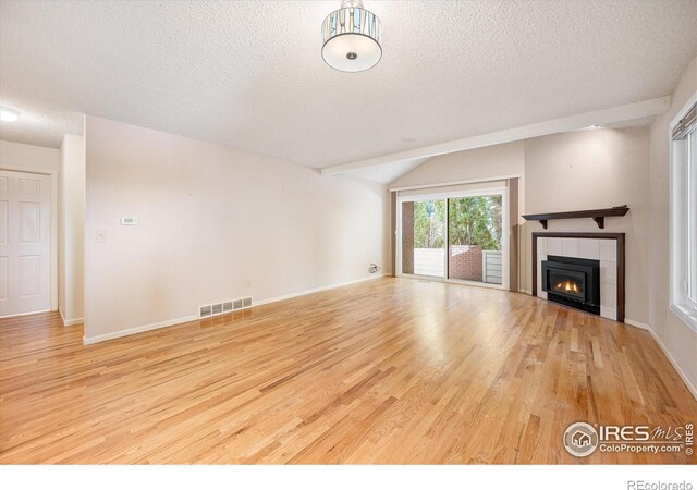 unfurnished living room featuring a fireplace, lofted ceiling, a textured ceiling, and light wood-type flooring