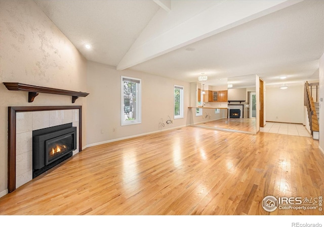 unfurnished living room with baseboards, a fireplace, lofted ceiling with beams, and light wood finished floors