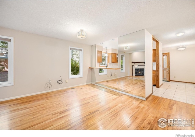 unfurnished living room with a textured ceiling, light wood finished floors, plenty of natural light, and a fireplace