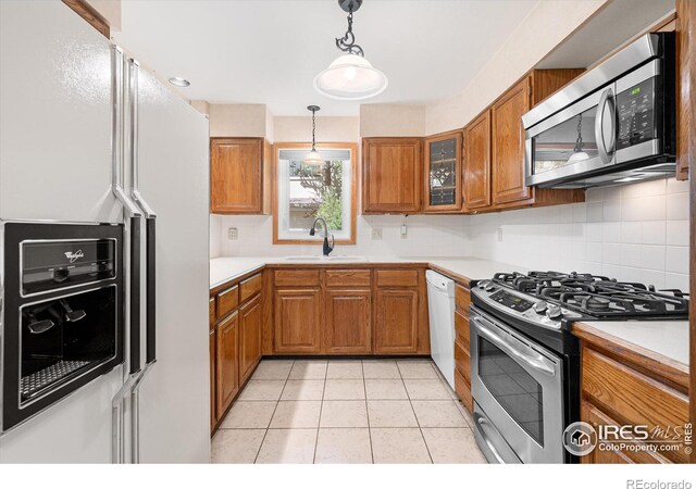 kitchen with pendant lighting, brown cabinets, light countertops, appliances with stainless steel finishes, and a sink