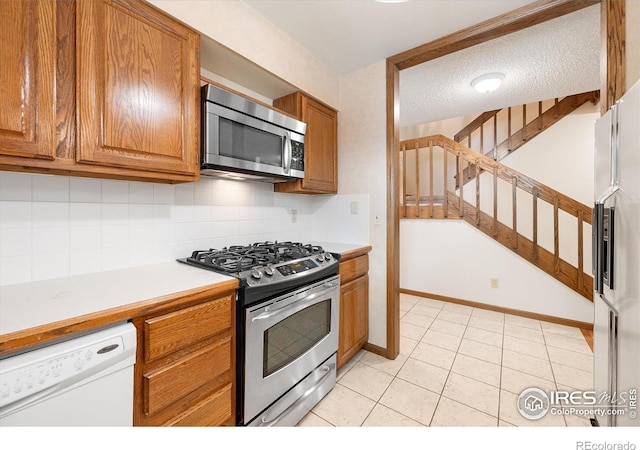 kitchen featuring decorative backsplash, brown cabinets, stainless steel appliances, a textured ceiling, and light countertops