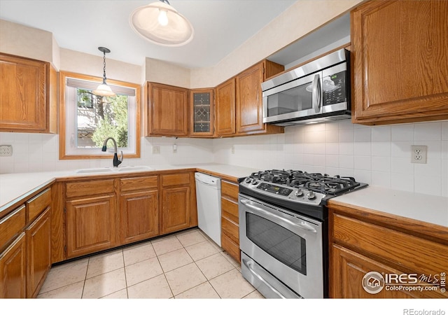 kitchen featuring brown cabinets, light countertops, appliances with stainless steel finishes, glass insert cabinets, and a sink