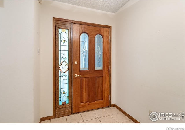 foyer entrance with a textured ceiling, light tile patterned floors, and baseboards