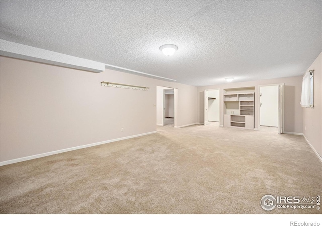 below grade area with light carpet, a textured ceiling, and baseboards