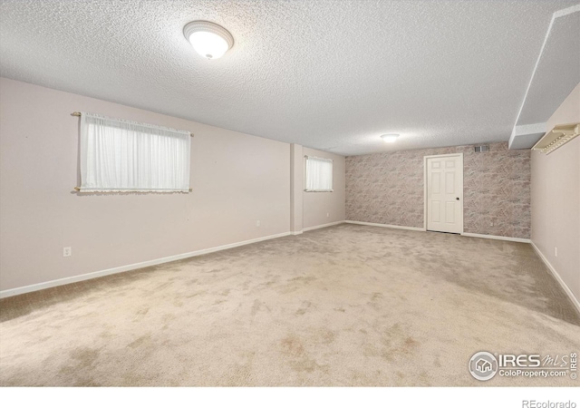 basement with carpet floors, visible vents, baseboards, and a textured ceiling