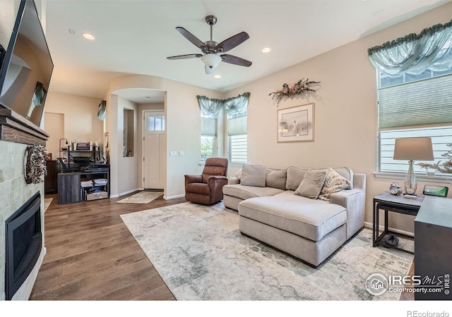 living room with ceiling fan, a tiled fireplace, and hardwood / wood-style floors