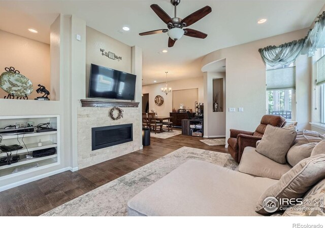 living room featuring ceiling fan with notable chandelier, a stone fireplace, and dark hardwood / wood-style flooring