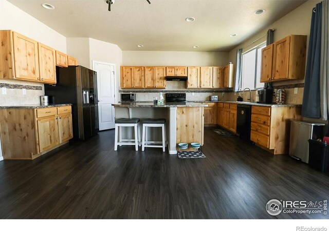 kitchen featuring decorative backsplash, dark hardwood / wood-style floors, a kitchen island, a breakfast bar area, and black appliances