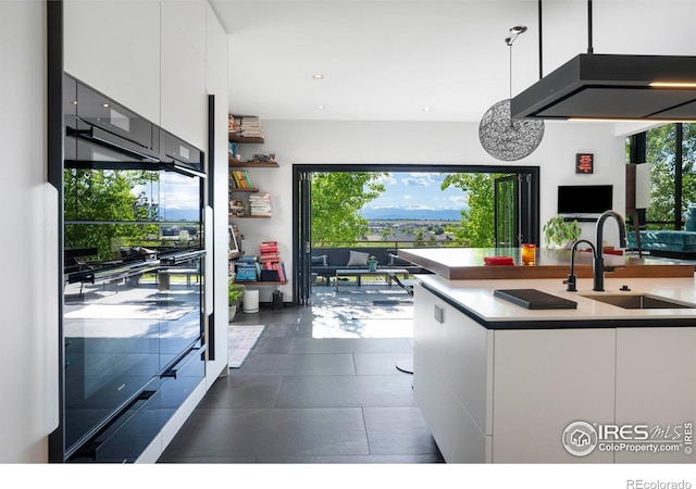 kitchen with a healthy amount of sunlight, hanging light fixtures, sink, white cabinets, and fridge