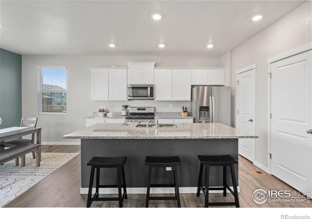 kitchen with hardwood / wood-style flooring, stainless steel appliances, a center island with sink, and white cabinets