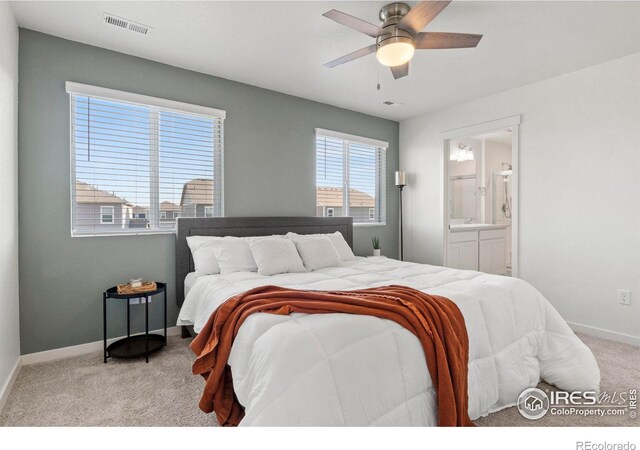 bedroom featuring ceiling fan, light colored carpet, and ensuite bath