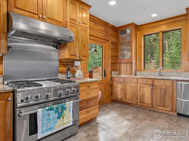 kitchen featuring high end stove, under cabinet range hood, light stone countertops, a sink, and glass insert cabinets