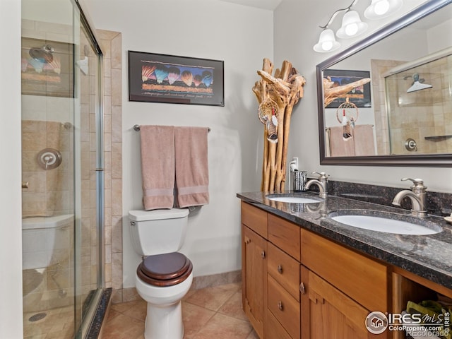 bathroom featuring tile patterned floors, a stall shower, toilet, double vanity, and baseboards
