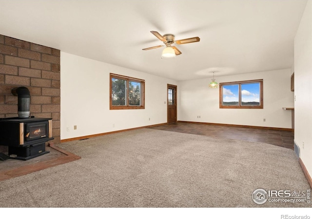 unfurnished living room with ceiling fan, a wood stove, and carpet