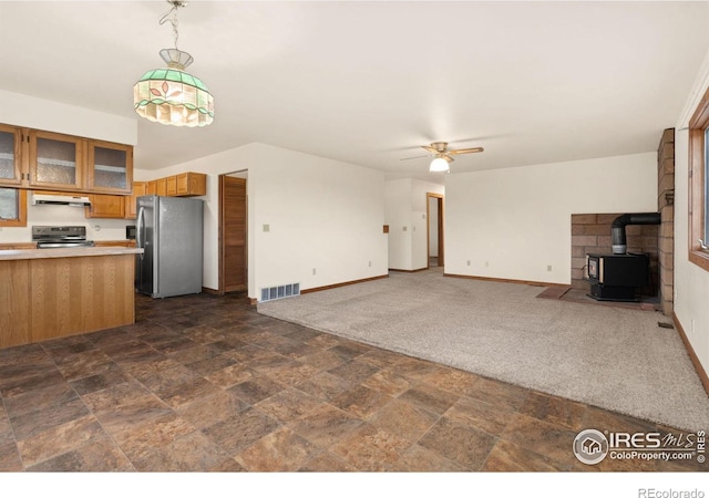 unfurnished living room featuring a wood stove, ceiling fan, and dark colored carpet