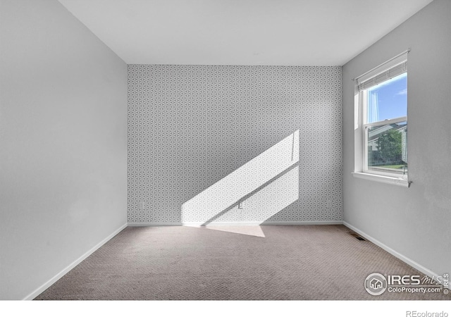 unfurnished room with an accent wall, carpet, baseboards, and wallpapered walls