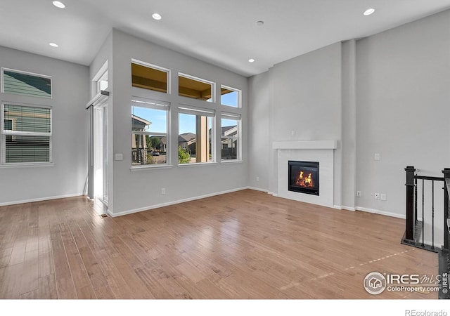 unfurnished living room with light wood finished floors, recessed lighting, baseboards, and a glass covered fireplace