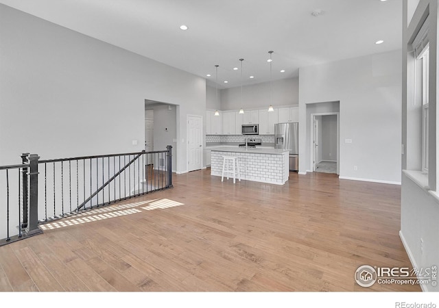 interior space featuring stainless steel appliances, light countertops, hanging light fixtures, a kitchen island with sink, and white cabinets