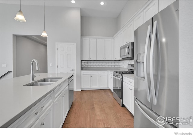 kitchen featuring white cabinets, hanging light fixtures, stainless steel appliances, light countertops, and a sink