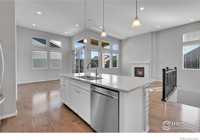 kitchen featuring a center island with sink, light countertops, hanging light fixtures, stainless steel dishwasher, and a sink