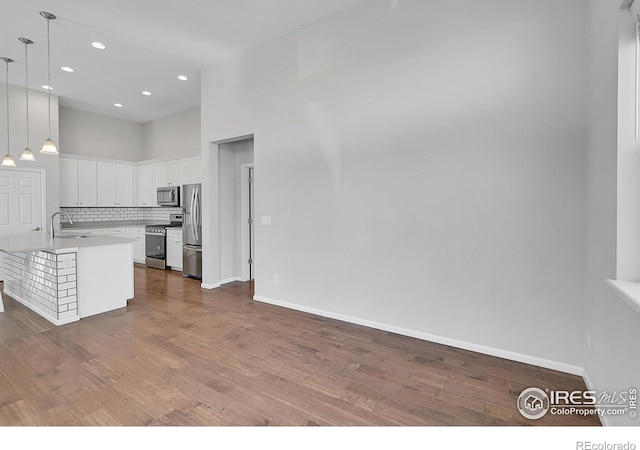 kitchen featuring white cabinets, light countertops, appliances with stainless steel finishes, hanging light fixtures, and an island with sink