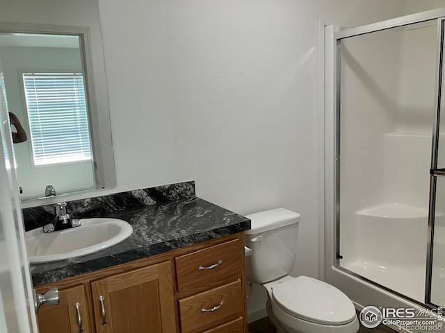 full bathroom with a shower with door, vanity, and toilet