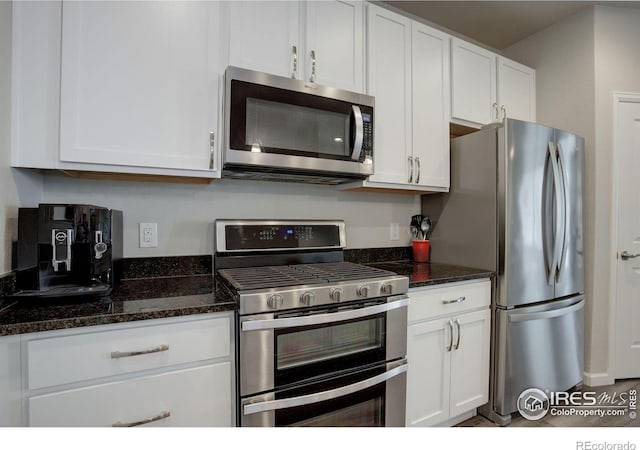 kitchen with dark stone countertops, stainless steel appliances, and white cabinetry