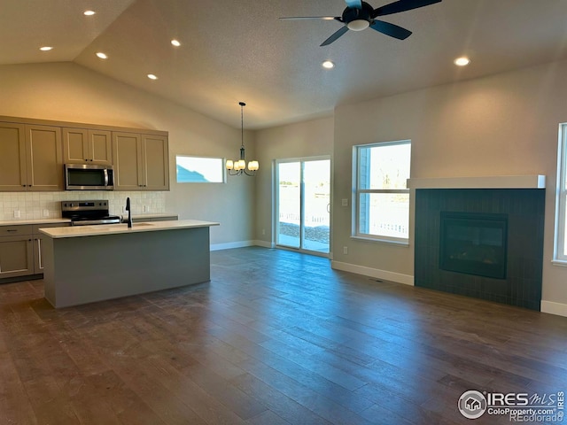 kitchen featuring decorative light fixtures, a tile fireplace, an island with sink, decorative backsplash, and stainless steel appliances