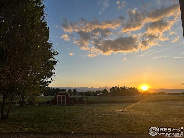 yard at dusk with a rural view, an outdoor structure, and a shed