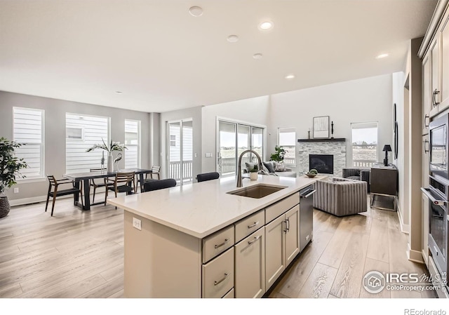 3140 Newfound Lake Rd, Berthoud, CO 80513 - kitchen featuring light countertops, a sink, a fireplace, light wood-type flooring, and a kitchen island with sink