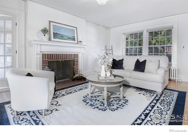 living room with radiator, a brick fireplace, and hardwood / wood-style flooring