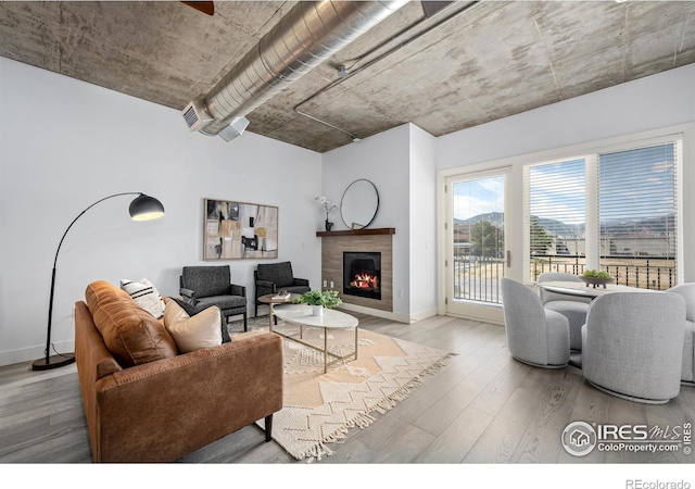 living room with a warm lit fireplace, baseboards, and wood finished floors