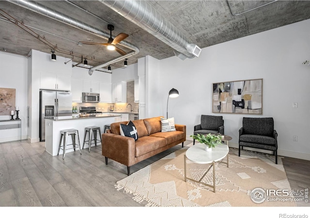 living room with baseboards, ceiling fan, a towering ceiling, and light wood finished floors