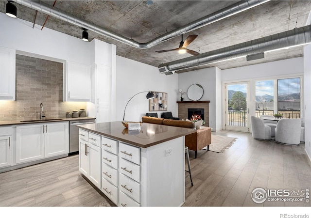 kitchen with dishwasher, dark countertops, open floor plan, a fireplace, and a sink