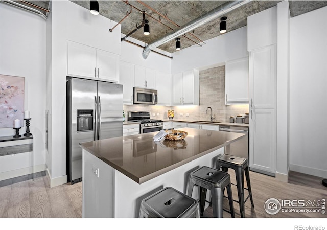 kitchen with light wood finished floors, stainless steel appliances, backsplash, white cabinets, and a kitchen bar