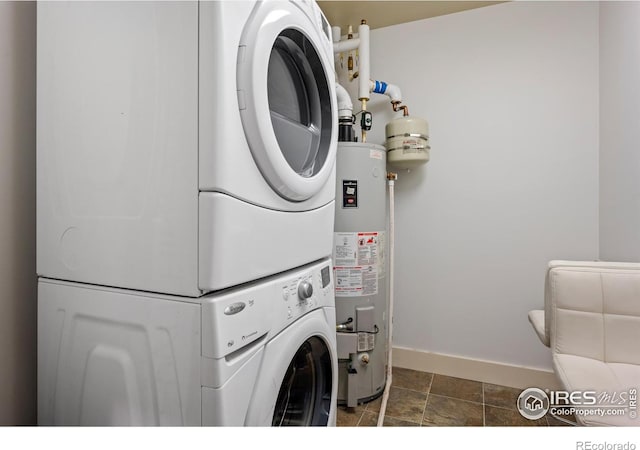 clothes washing area featuring laundry area, gas water heater, stacked washer and clothes dryer, and baseboards