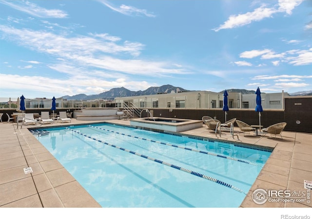 pool with a patio, a mountain view, and a hot tub