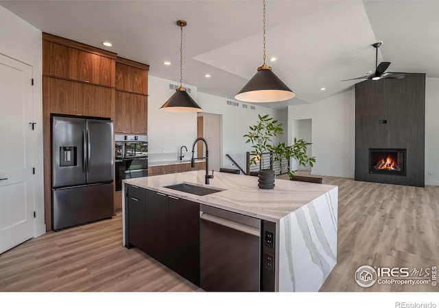 kitchen featuring a center island with sink, hanging light fixtures, sink, a fireplace, and appliances with stainless steel finishes