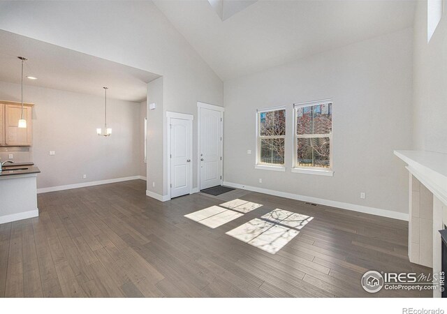 unfurnished living room featuring high vaulted ceiling, dark hardwood / wood-style floors, sink, and a tile fireplace